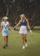 Two women walking on a golf course with golf clubs.