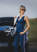 Woman in a blue outfit standing next to a black car with an open trunk.