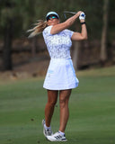 Woman playing golf on a green course with trees in the background