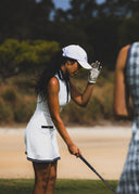 Woman in white golf attire preparing to hit a golf ball on a golf course.