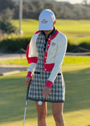 Person in a checkered dress and white cap holding a golf club on a golf course.